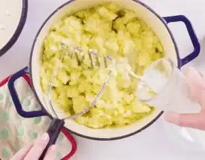 Add the milk to the mashed potatoes and continue mashing until everything is thoroughly combined for a creamier texture for Texas Roadhouse Mashed Potatoes Recipe.